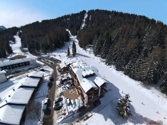 Veduta aerea di Folgarida con gli alberghi lungo la pista innevata e il bosco alle spalle