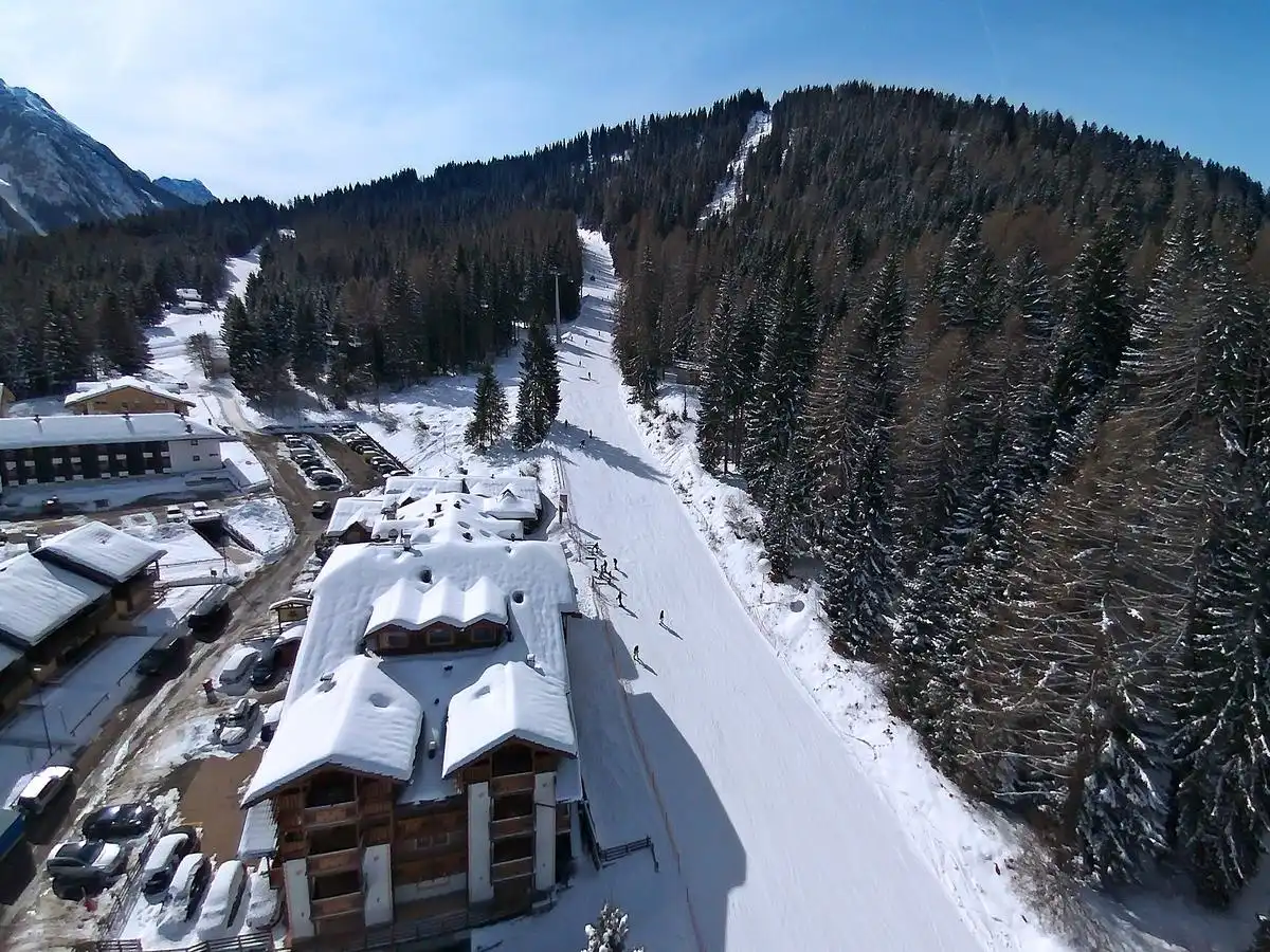 Vista dall'alto dell'Hotel Dal Bracconiere e della pista Azzurra tra i boschi di Folgarida