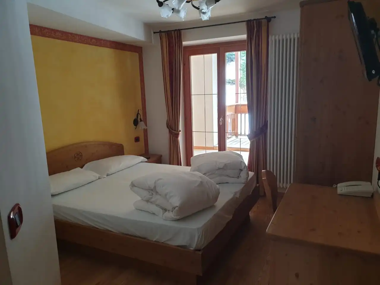 Letto matrimoniale con parete gialla, scrivania in legno e porta finestra sul terrazzo
