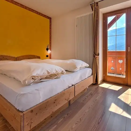 Letto matrimoniale con parete gialla e porta finestra sul terrazzo soleggiato
