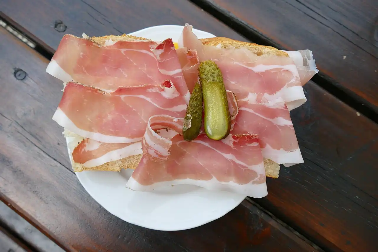 Un piatto di speck affettato servito con pane e cetriolini su un tavolo di legno
